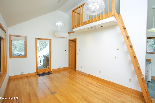 unfurnished living room with a wall mounted air conditioner, wood finished floors, high vaulted ceiling, a chandelier, and stairs
