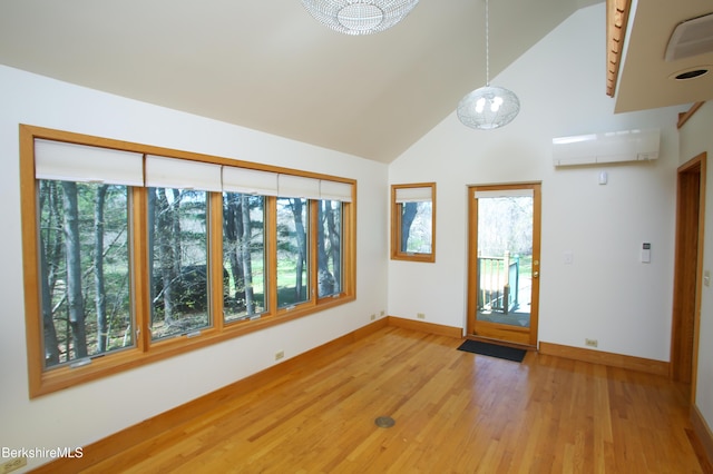 interior space featuring light wood-style floors, high vaulted ceiling, baseboards, and a wall unit AC