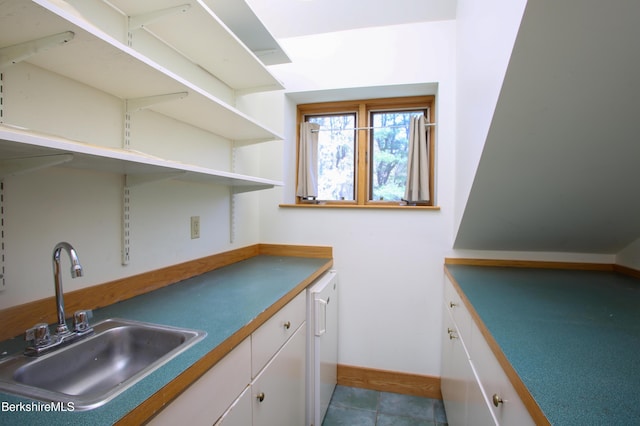 interior space with a sink, baseboards, and white cabinets