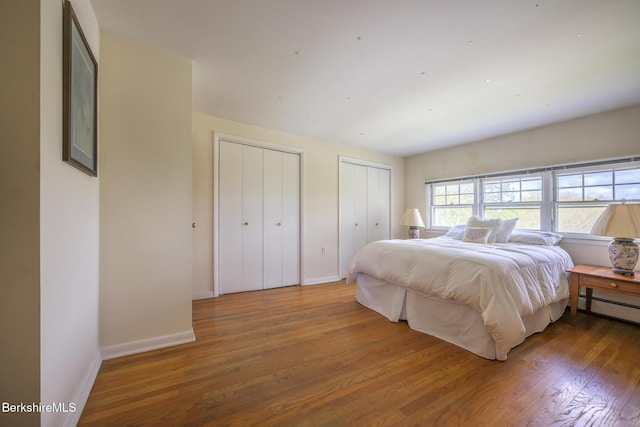 bedroom featuring two closets, baseboards, and wood finished floors