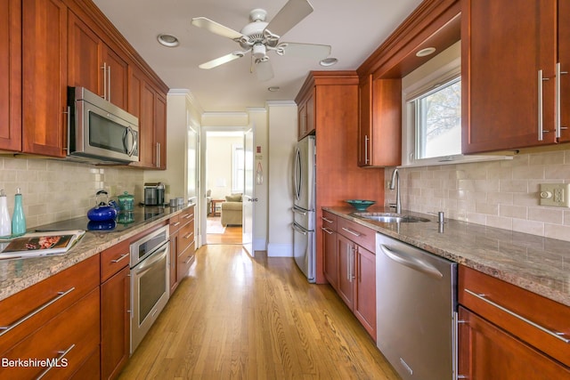 kitchen with a sink, stone countertops, tasteful backsplash, light wood-type flooring, and appliances with stainless steel finishes