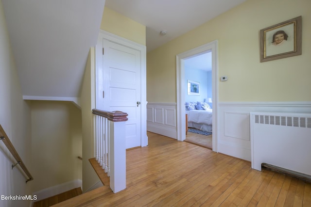 hall with radiator, a decorative wall, a wainscoted wall, light wood-type flooring, and an upstairs landing
