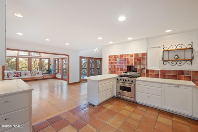 kitchen with backsplash, kitchen peninsula, white cabinetry, and luxury stove