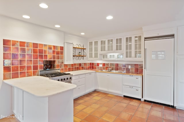 kitchen with stainless steel range, sink, tasteful backsplash, kitchen peninsula, and white cabinets