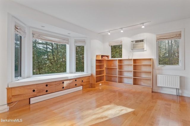 unfurnished room featuring a wealth of natural light, radiator, a wall mounted AC, a baseboard heating unit, and wood-type flooring