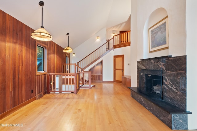 living room featuring light wood-type flooring, a stone fireplace, and wooden walls