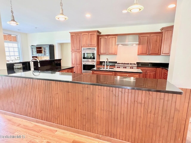 121 E Dugway Rd, Lenox, MA 01240 - kitchen featuring wall chimney exhaust hood, stainless steel double oven, decorative light fixtures, light wood finished floors, and a kitchen island with sink