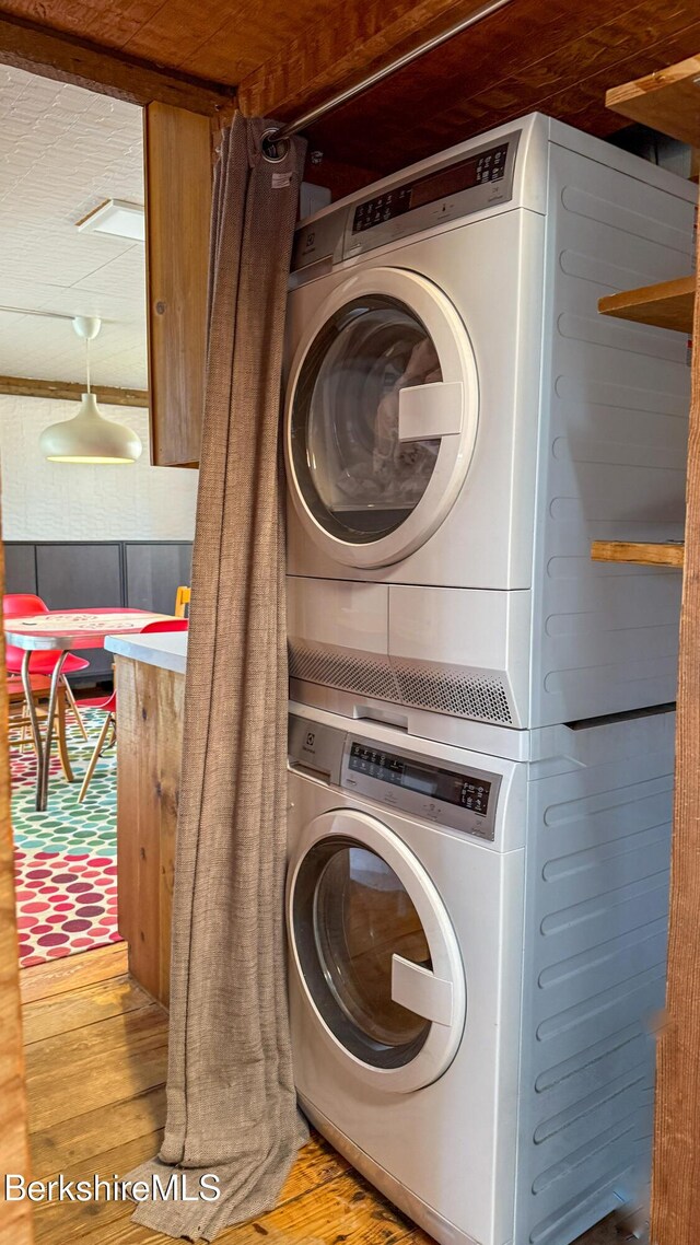 clothes washing area featuring laundry area, stacked washing maching and dryer, and wood finished floors