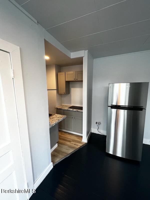 kitchen featuring black stovetop, light wood-style floors, freestanding refrigerator, light stone countertops, and baseboards