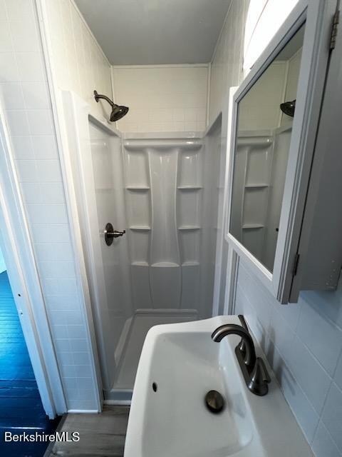 bathroom with a sink, a shower stall, and tile walls