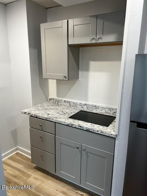 kitchen with light stone countertops, black electric stovetop, gray cabinets, and freestanding refrigerator