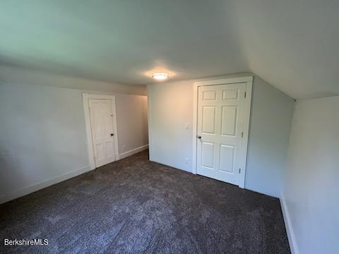 bonus room with baseboards, dark carpet, and vaulted ceiling