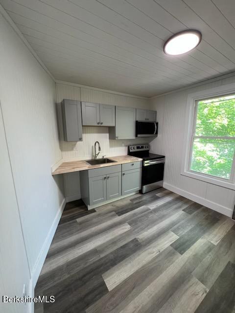 kitchen featuring wood finished floors, gray cabinets, stainless steel appliances, light countertops, and a sink