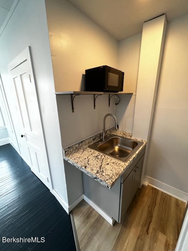 kitchen with black microwave, open shelves, dark wood-type flooring, and a sink