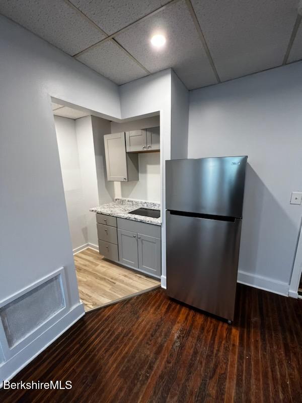 kitchen with a paneled ceiling, dark wood finished floors, freestanding refrigerator, and gray cabinetry