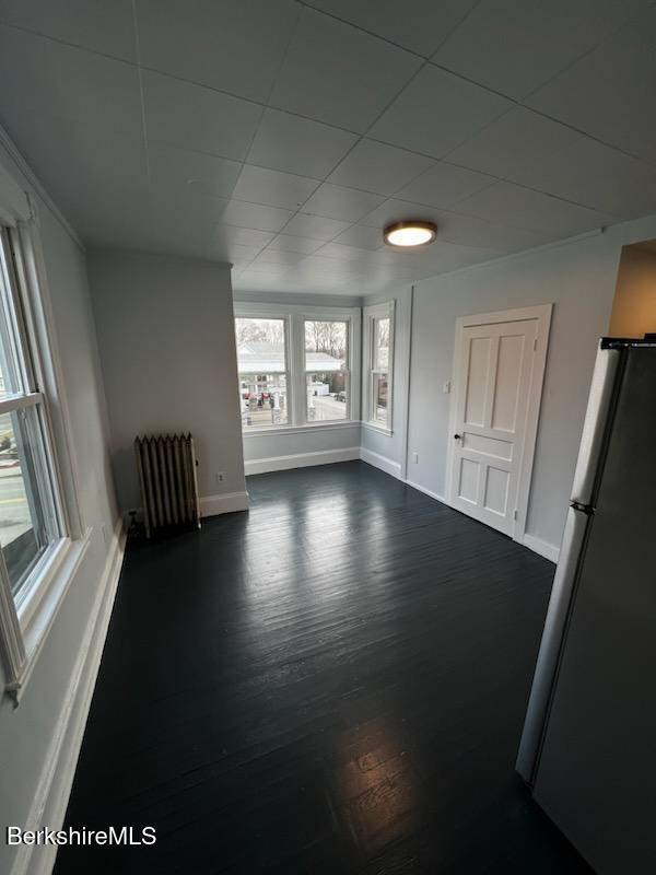 spare room featuring dark wood-type flooring, radiator heating unit, and baseboards