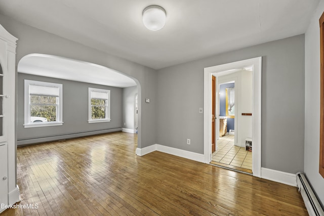 empty room featuring hardwood / wood-style floors, baseboards, arched walkways, and a baseboard radiator