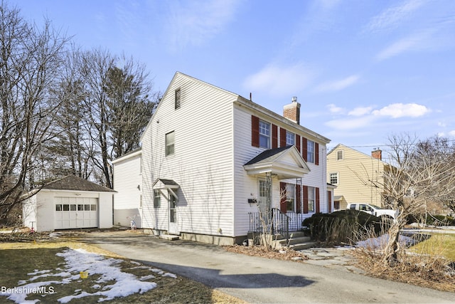 view of front of home with aphalt driveway, a chimney, a detached garage, and an outdoor structure