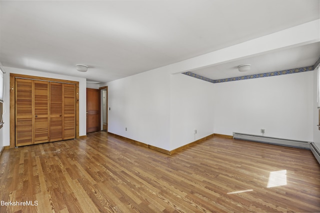 unfurnished bedroom with a closet, baseboards, wood finished floors, and a baseboard radiator