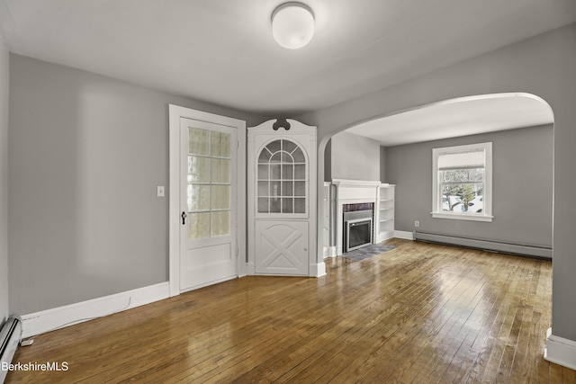 unfurnished living room featuring a fireplace, a baseboard heating unit, baseboards, and wood-type flooring