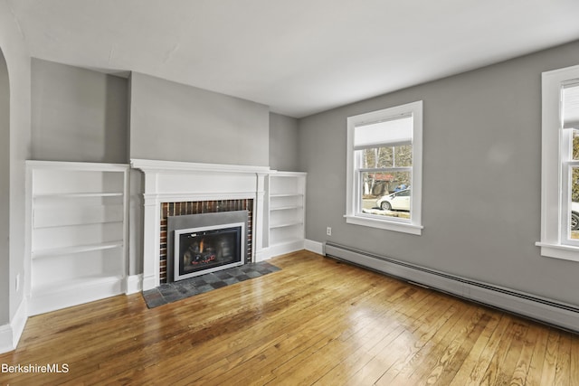 unfurnished living room with a fireplace, a baseboard heating unit, baseboards, and hardwood / wood-style floors