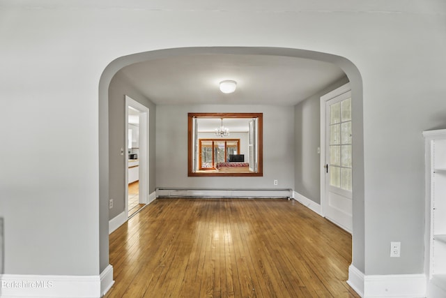 empty room featuring a baseboard heating unit, a healthy amount of sunlight, arched walkways, and wood-type flooring