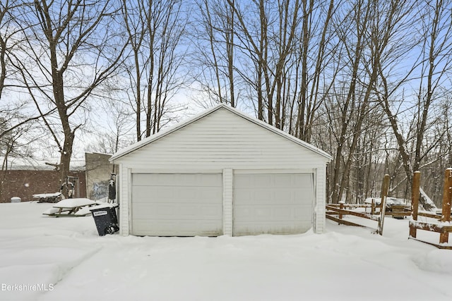 snow covered garage featuring a garage and fence