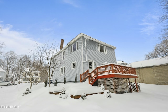 snow covered house featuring a deck and a chimney