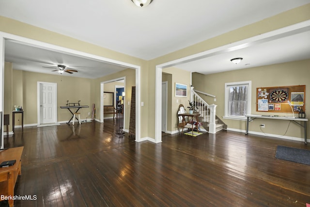 empty room with stairs, wood finished floors, a ceiling fan, and baseboards