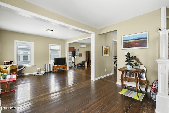 living area featuring dark wood-style floors, radiator heating unit, decorative columns, and baseboards