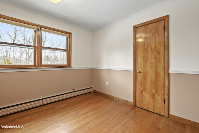 spare room with a baseboard radiator, baseboards, ornamental molding, and light wood-style flooring