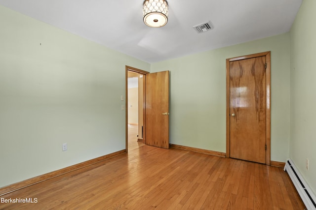 unfurnished bedroom featuring light wood-style floors, visible vents, baseboard heating, and baseboards