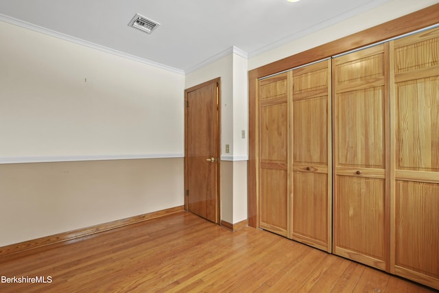 unfurnished bedroom featuring visible vents, a closet, crown molding, light wood finished floors, and baseboards