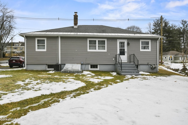 snow covered back of property with entry steps, a chimney, and roof with shingles