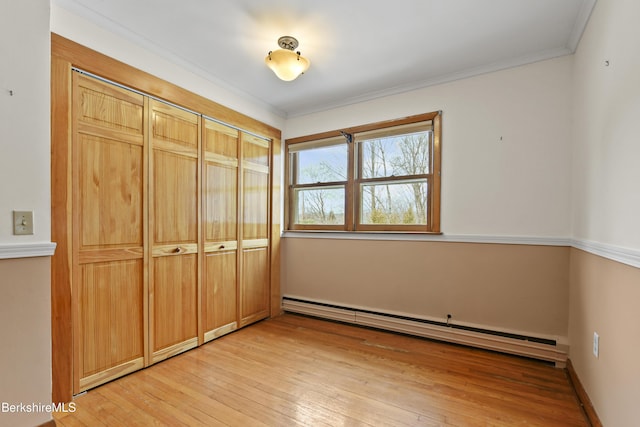 unfurnished bedroom with ornamental molding, a baseboard heating unit, a closet, light wood finished floors, and baseboards