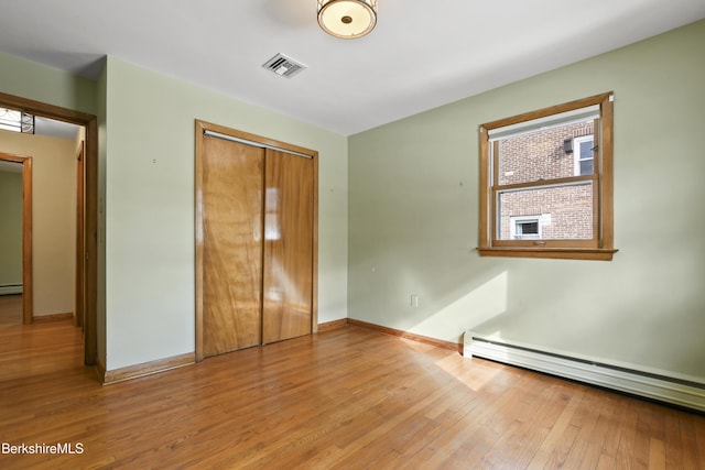 unfurnished bedroom featuring visible vents, baseboards, baseboard heating, a closet, and wood-type flooring