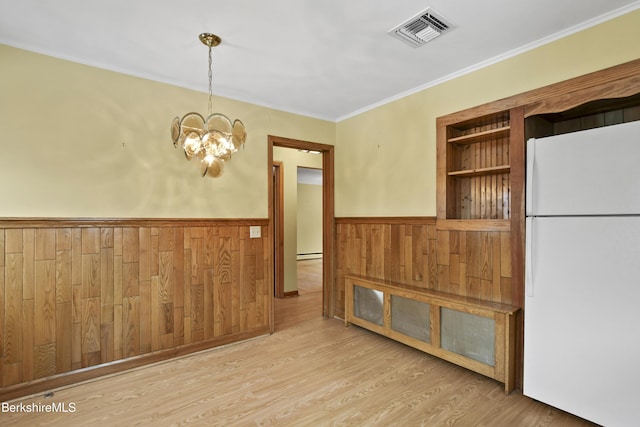 unfurnished room featuring visible vents, crown molding, a wainscoted wall, wood finished floors, and a notable chandelier