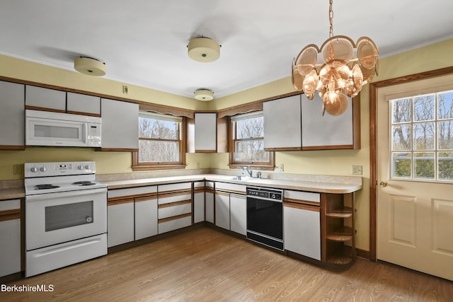 kitchen with light countertops, an inviting chandelier, light wood-style floors, white appliances, and a sink