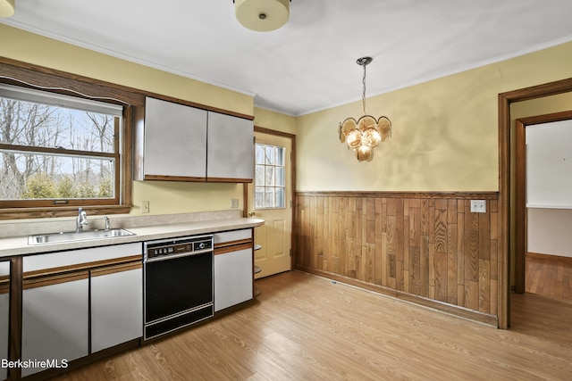 kitchen with light wood-style flooring, a sink, black dishwasher, wainscoting, and light countertops