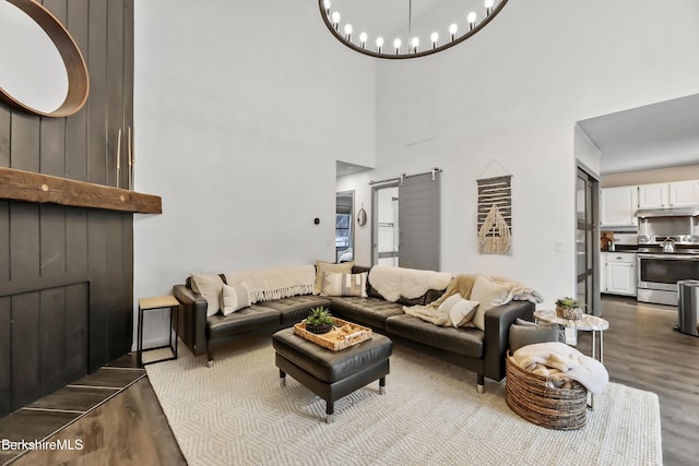 living room featuring a towering ceiling, a barn door, a chandelier, and light wood-type flooring