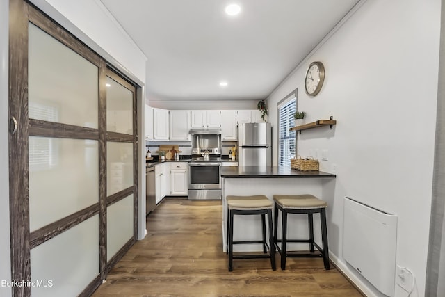 kitchen featuring dark wood-type flooring, a breakfast bar area, white cabinetry, kitchen peninsula, and stainless steel appliances