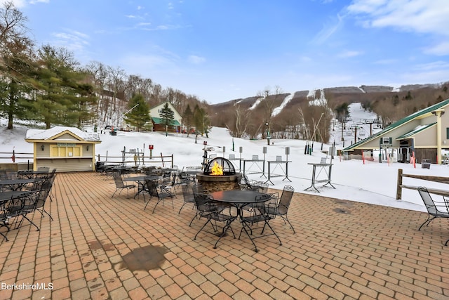 snow covered patio featuring a mountain view and an outdoor fire pit