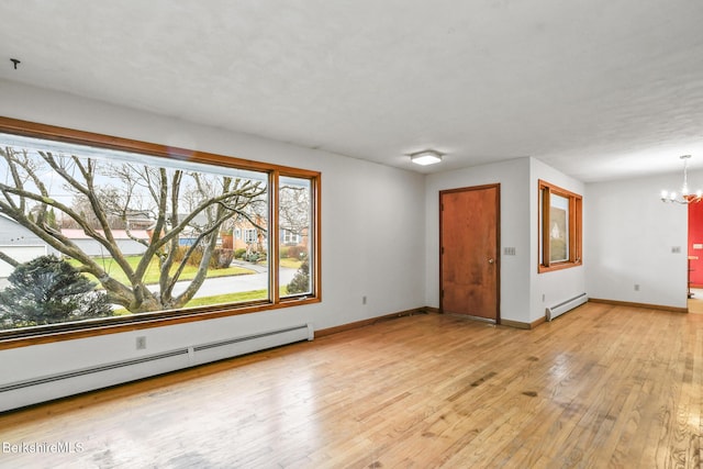 empty room featuring light hardwood / wood-style flooring, a chandelier, and a baseboard heating unit