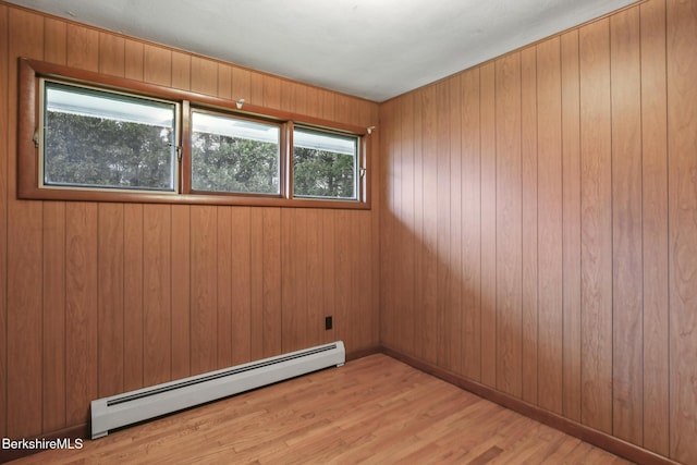 unfurnished room with wood walls, light wood-type flooring, and a baseboard heating unit