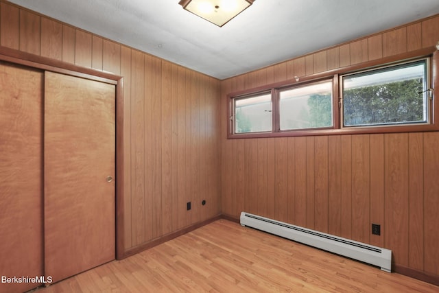 unfurnished bedroom with wooden walls, light hardwood / wood-style flooring, a closet, and a baseboard heating unit