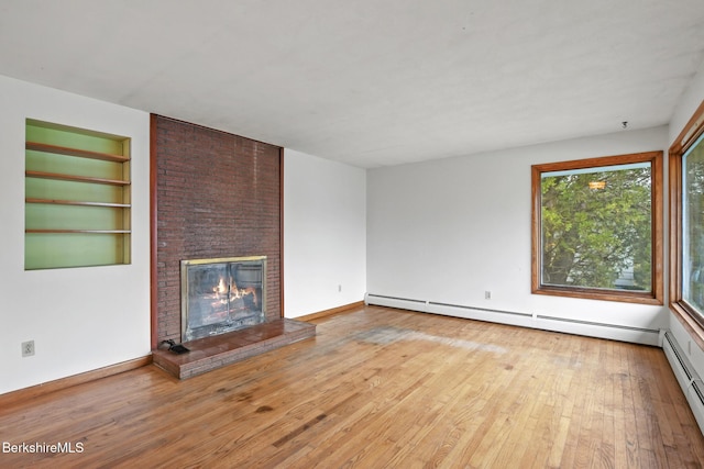 unfurnished living room with built in shelves, light wood-type flooring, a baseboard heating unit, and a brick fireplace