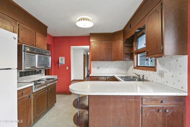 kitchen with kitchen peninsula, a kitchen breakfast bar, stainless steel gas cooktop, sink, and white fridge