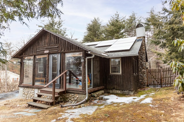 view of front of property featuring solar panels, a shingled roof, fence, a sunroom, and a chimney