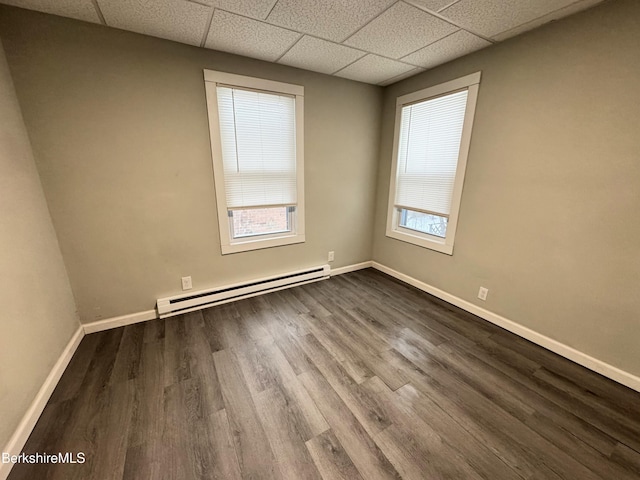 empty room with a baseboard radiator, wood-type flooring, and a drop ceiling