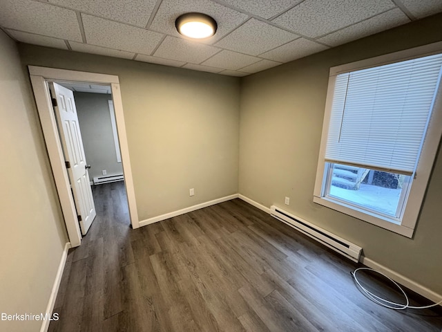 empty room with a baseboard heating unit, a drop ceiling, and dark hardwood / wood-style flooring